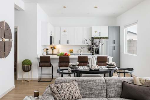 A modern living room with a grey couch and a kitchen in the background.