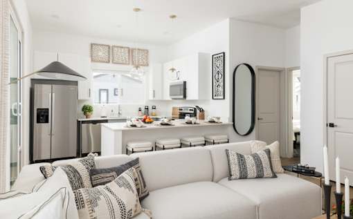 A modern living room with a white couch and a kitchen area in the background.