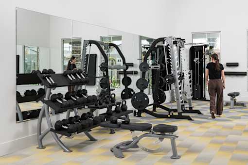 A woman is walking in a gym with a variety of exercise equipment.