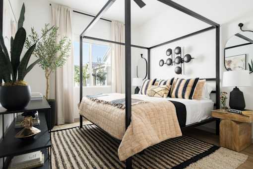 A bedroom with a four poster bed and a cactus on the side table.