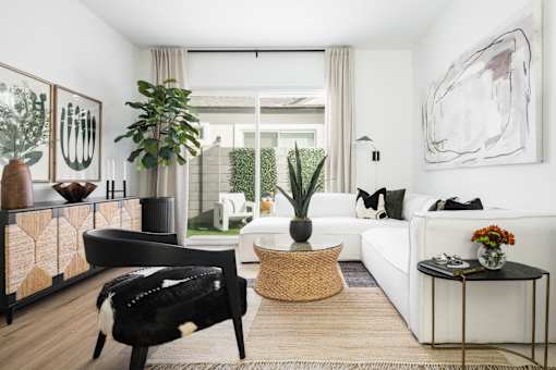 A living room with a black and white chair, a wicker basket, a white sofa, and a large painting on the wall.