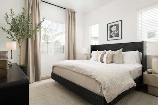A bedroom with a large bed and a tree in a vase.