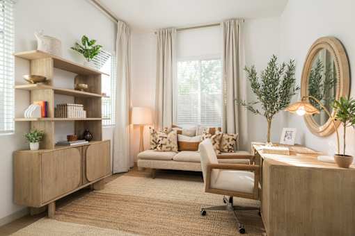 A well-lit, cozy room with a couch, chair, desk, and a bookshelf.