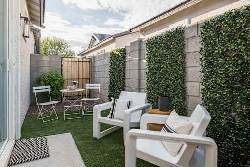 A white chair is in the foreground of a backyard with a table and a speaker.