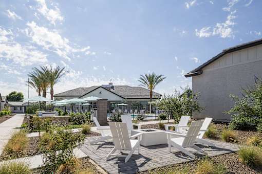 A patio with white chairs and a table is surrounded by plants and trees.