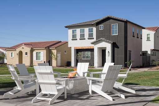 A patio with white chairs and a fire pit in front of a house.
