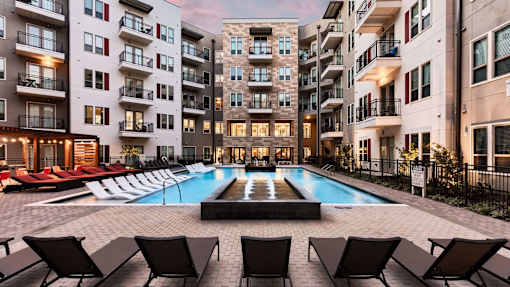 A swimming pool surrounded by lounge chairs in front of apartment buildings.