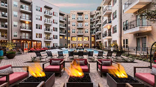 A fire pit in the middle of a courtyard surrounded by chairs and buildings.