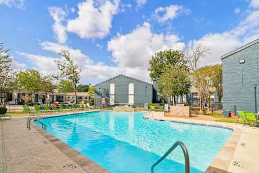 A swimming pool surrounded by a concrete deck and a grassy area with trees.