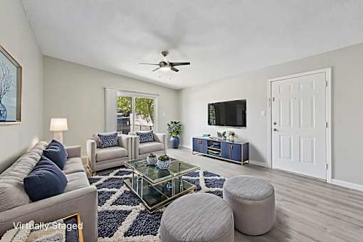 A living room with a grey sofa, a glass coffee table, and a ceiling fan.