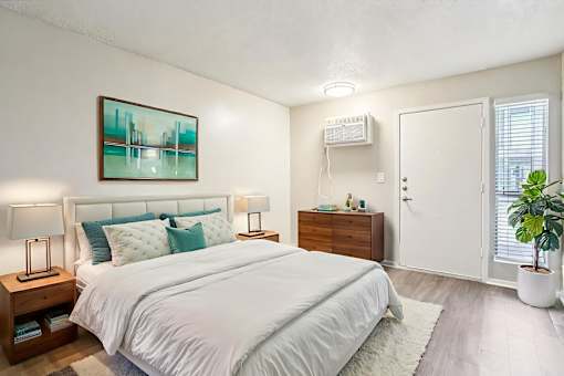 A bedroom with a large bed, a nightstand with a lamp, and a painting on the wall.