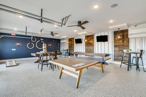 A ping pong table is in the middle of a room with a blue wall and a ceiling fan.