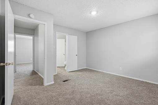 A room with white walls and carpeted floor with two doors.