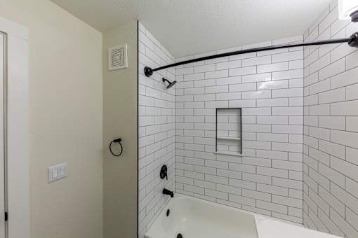 A white tiled shower with a white tub and a black shower head.