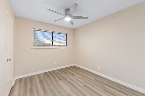 an empty bedroom with a ceiling fan and a window
