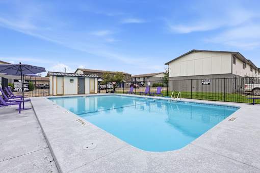 A large outdoor swimming pool with purple lounge chairs.