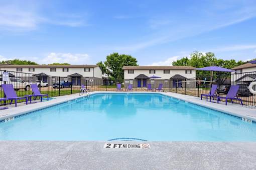 A 2 ft deep swimming pool with purple loungers and a fence around the pool area.