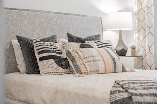 A bed with a grey headboard and striped pillows.