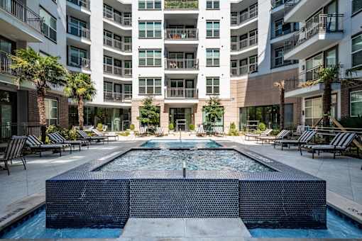 A large pool in the middle of a courtyard surrounded by lounge chairs and palm trees.