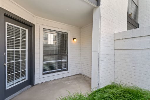 a patio with a black door and a window with venetian blinds