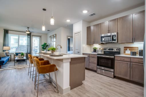 a kitchen with a large center island with a breakfast bar and a living room in the background