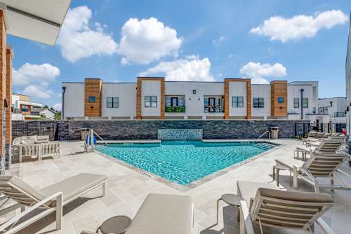 A pool area with sun loungers and a building in the background.