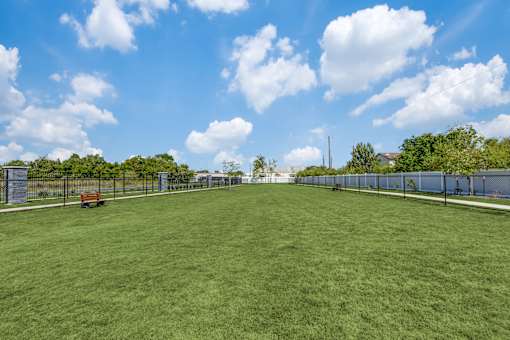 A large, open grassy field with a fence on either side and a bench in the middle.