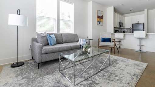 A modern living room with a grey sofa and a glass coffee table.