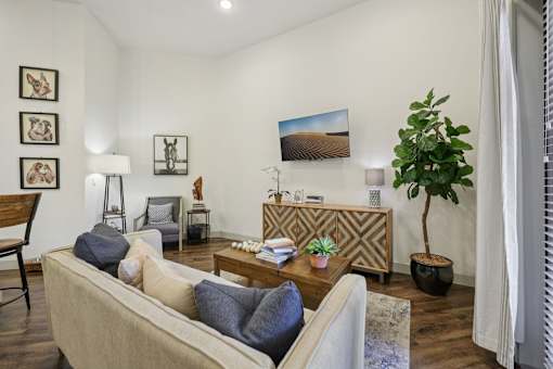 A spacious, open living room with expansive eggshell-colored walls and contrasting dark hardwood floors, brightly lit by natural light.