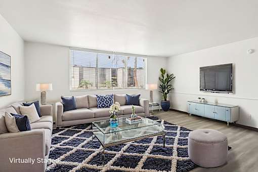 A living room with a glass coffee table and a large window.