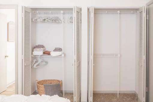 a walk in closet with white closet doors and a white bed with a basket