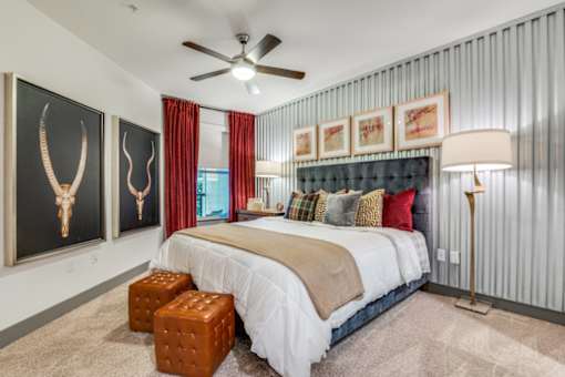 A bedroom with a bed, a ceiling fan, and a painting of an animal skull on the wall.