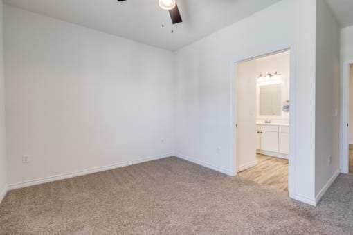 a bedroom with white walls and carpet and a door to a bathroom