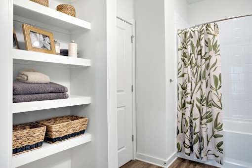 A white bathroom with a shower curtain and towels on the shelves.