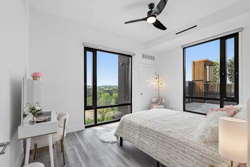 A bedroom with a large bed, a desk, and a balcony with a view of a building.