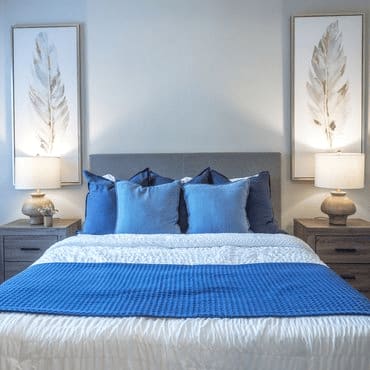 A bed with a blue comforter and pillows is flanked by two lamps on nightstands.