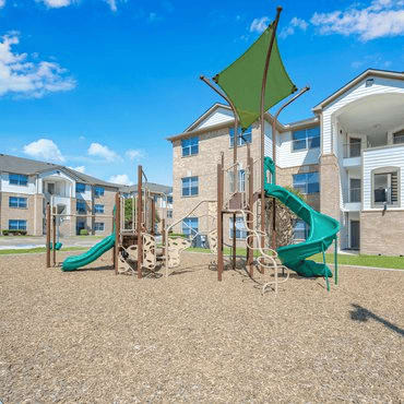 A playground with a green slide and a wooden swing set.