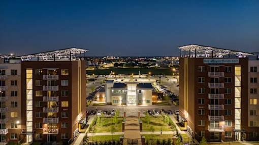 A view of a cityscape at night with two large buildings on the left and a parking lot in the middle.