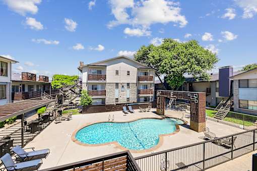 A pool surrounded by a fence and chairs in front of a building.