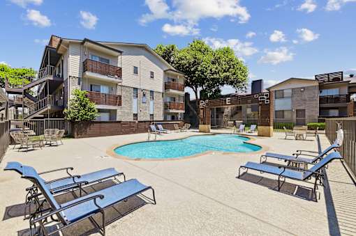A pool surrounded by lounge chairs in front of apartment buildings.