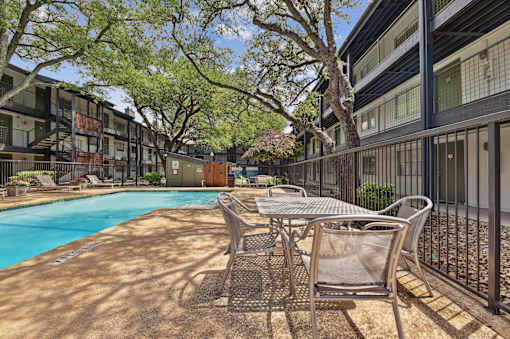 A pool surrounded by chairs and trees in a sunny courtyard.