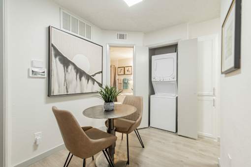A dining room with a table and chairs and a framed artwork on the wall.