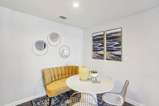 A yellow chair sits in front of a white table with a vase on it.