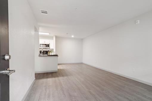 A room with a wooden floor and a kitchenette in the background.