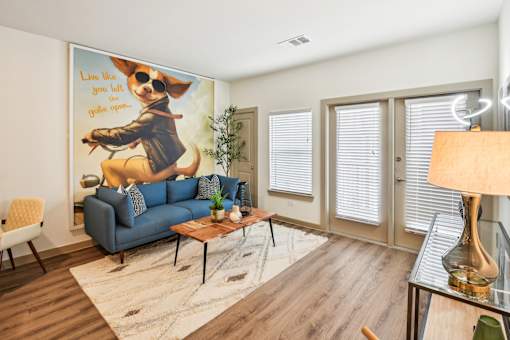 A living room with a blue couch and a poster of a dog on the wall.