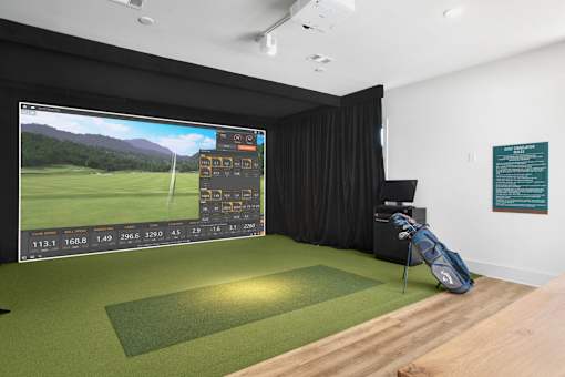 A golf simulator room with a screen showing a golf course and a bag of clubs on the floor.