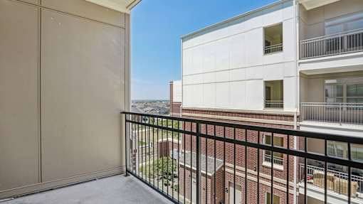 A balcony with a black railing overlooks a building and a clear blue sky.