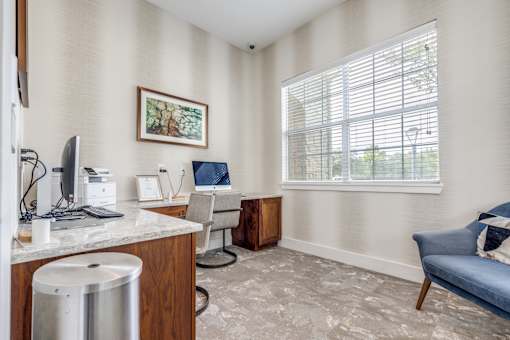 A room with a desk, chair, and a window with blinds.