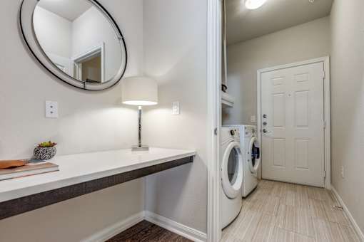 A laundry room with a washer and dryer, a counter, and a round mirror.