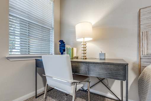 A white chair sits in front of a desk with a lamp on it.